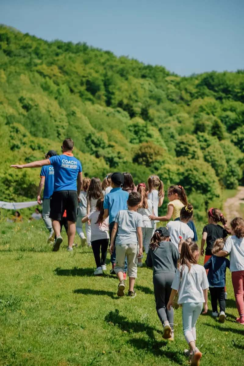A class walks single file up a grassy hillside path on a sunny day