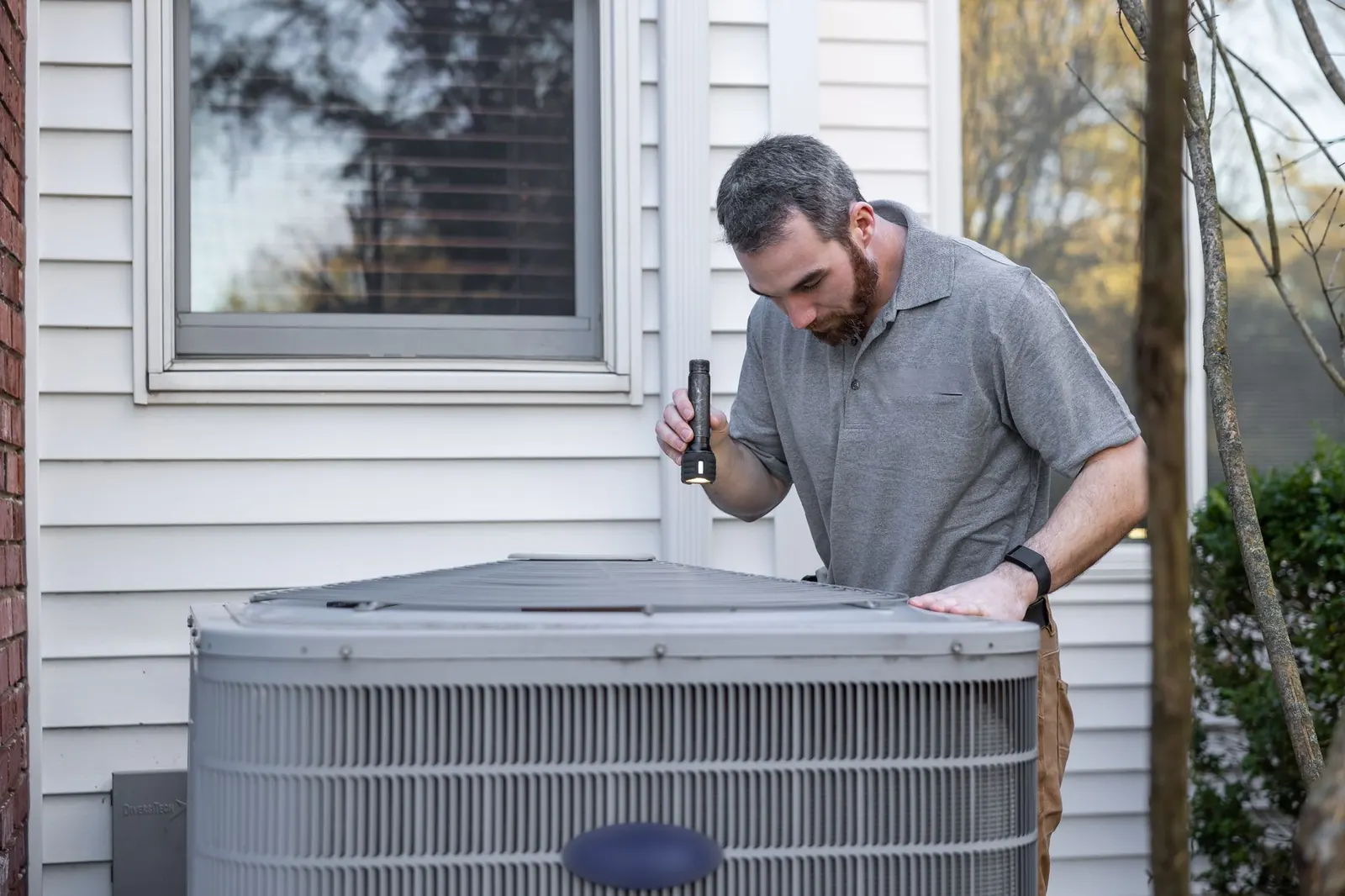 Technician checking an outdoor air conditioning unit beside a house