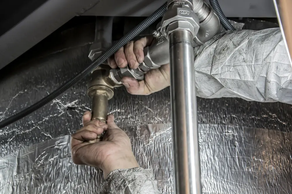 Hands tightening a fitting on pipes under a sink